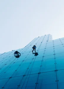 vertical-low-angle-shot-two-people-climbing-tall-glass-building-day-time